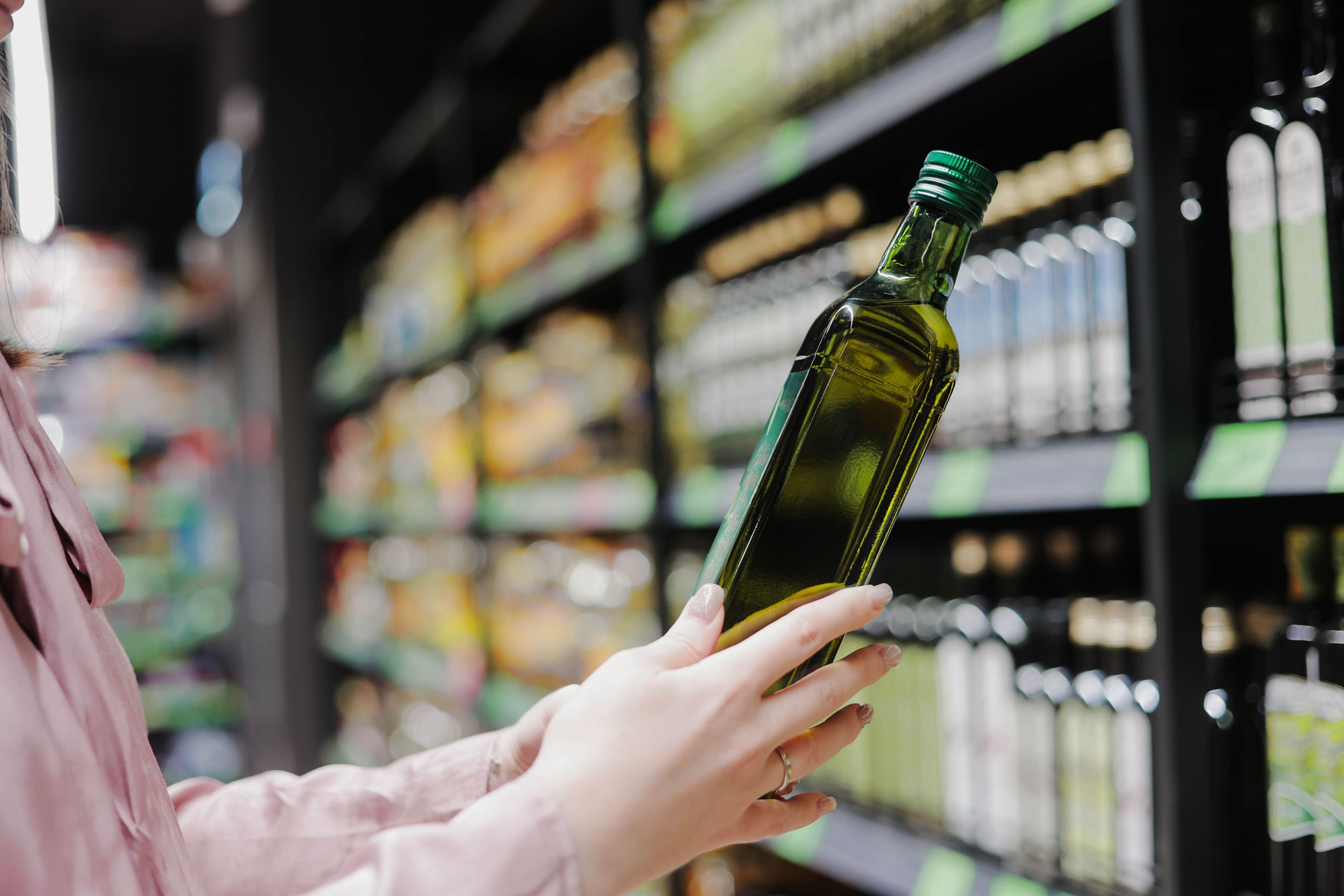 Persona coge aceite de oliva en el supermercado