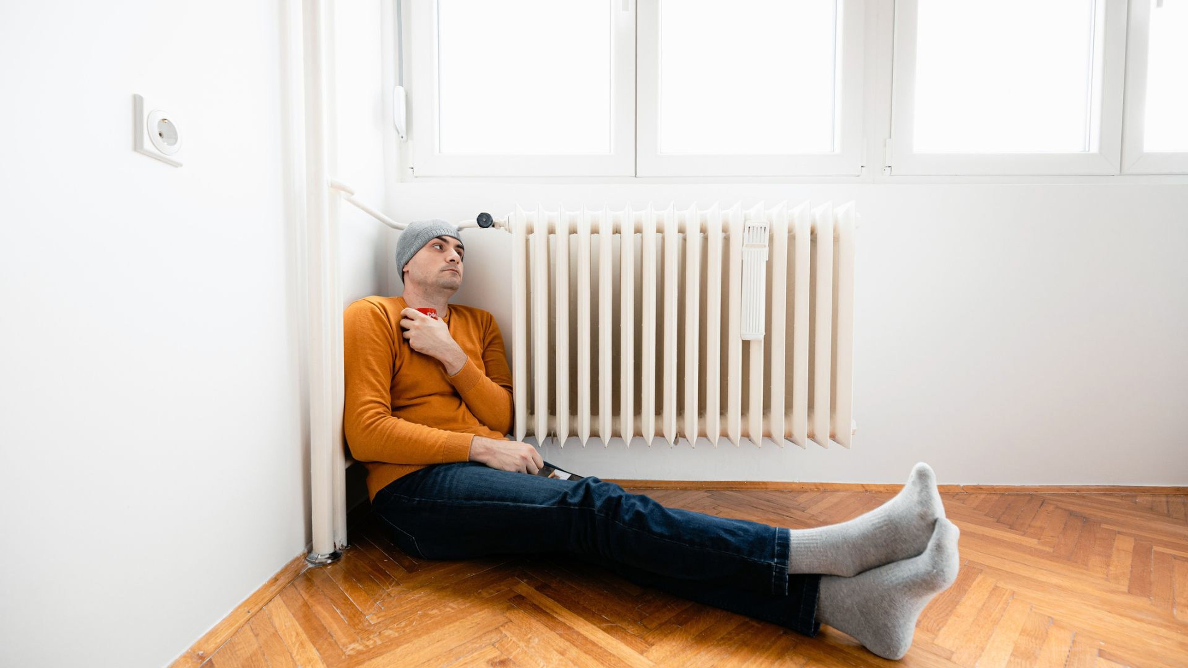 Una persona sentada en el suelo de su casa vacía al lado del radiador.