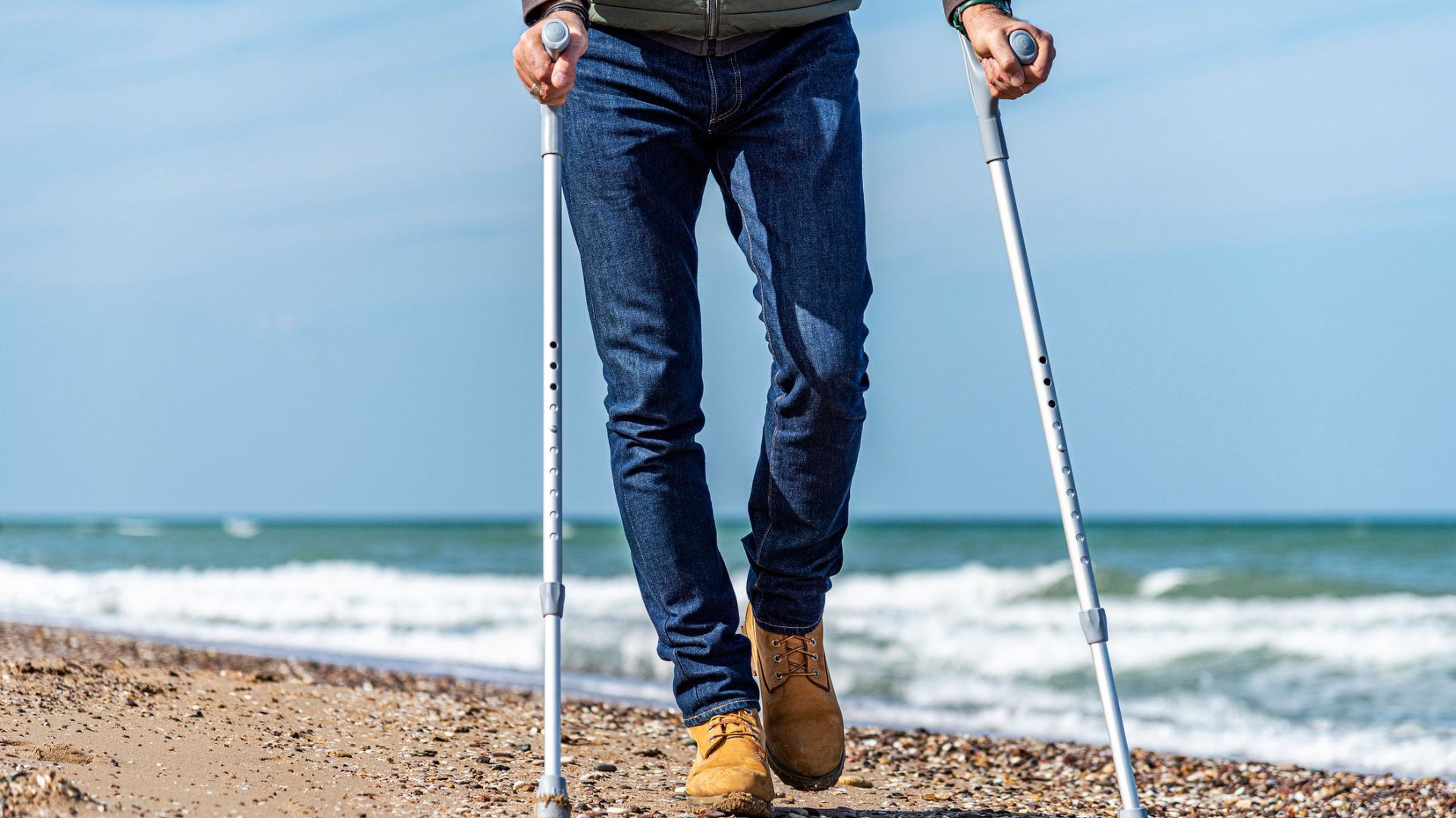 Un hombre con muletas pasea por la playa.