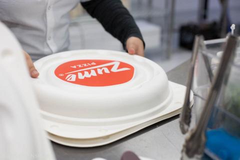 A human packages the order in an untraditional pizza delivery box, made from sustainably farmed sugarcane fiber, which is recyclable and compostable.