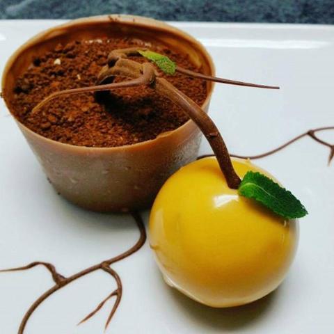 Una maceta de chocolate rellena de mousse de chocolate con ramas de árboles de chocolate y una naranja rellena con zumo de naranja recién exprimido.