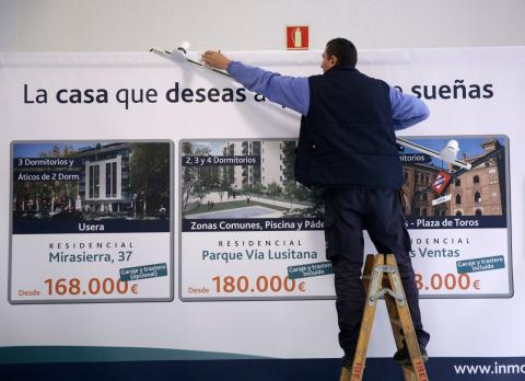 Un operario desmonta un cartel de viviendas en venta en Madrid