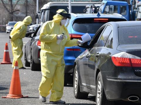 Medical members wearing protective gear guide drivers at a "drive-through" virus test facility in Goyang, north of Seoul, on February 29, 2020.