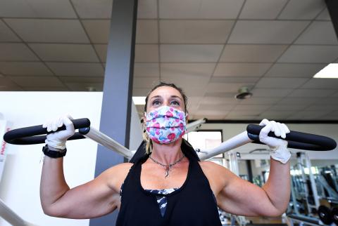 Mujer haciendo pesas con mascarilla y guantes en un gimnasio. 