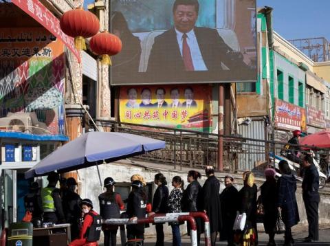In this Nov. 3, 2017, photo, residents walk through a security checkpoint into the Hotan Bazaar where a screen shows Chinese President Xi Jinping in Hotan in western China's Xinjiang region. In this Nov. 3, 2017, photo, residents walk through a security checkpoint into the Hotan Bazaar where a screen shows Chinese President Xi Jinping in Hotan in western China's Xinjiang region.
