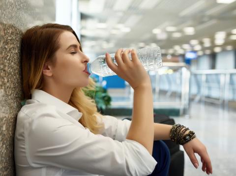 Una chica bebe agua de una botella de plástico en un aeropuerto Una chica bebe agua de una botella de plástico en un aeropuerto