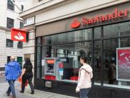 People walk on a sidewalk outside of a Santander branch with an ATM