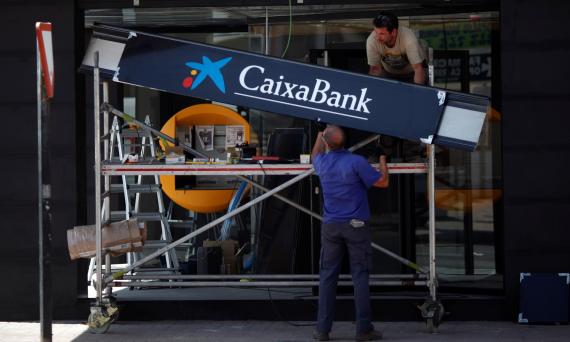 Dos trabajadores colocan el letrero de CaixaBank en una sucursal en Málaga