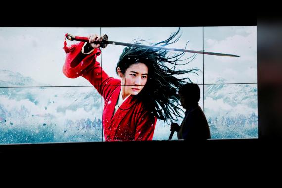Una persona pasa por delante de una pantalla con Mulan en Pekín, última película de Disney estrenada en Disney Plus. 